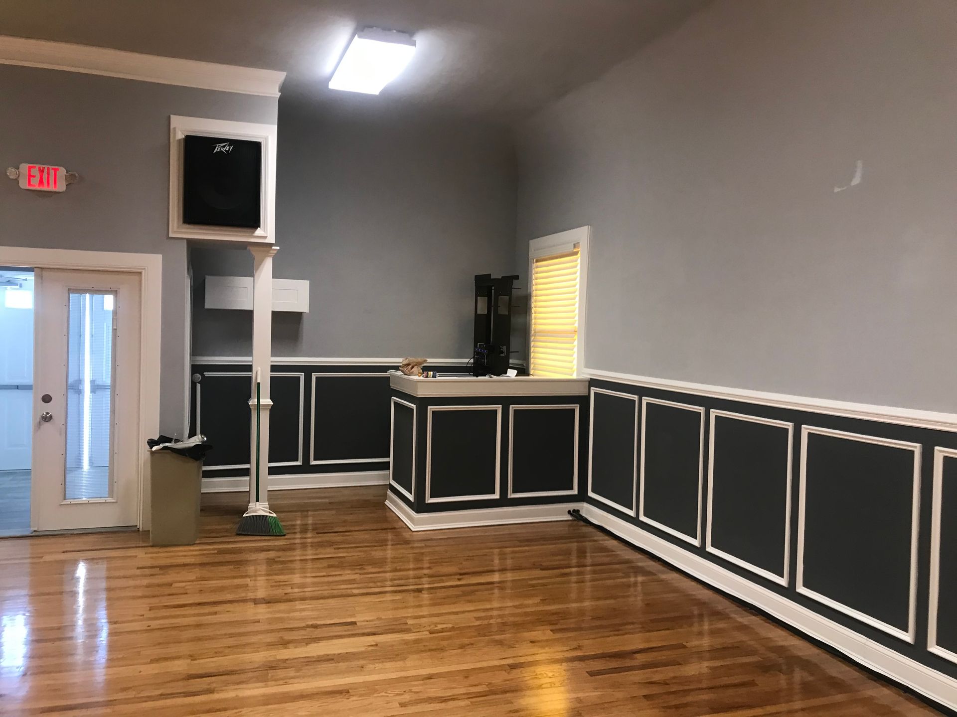 Empty hall with polished wood floor, gray walls, black trim, and a doorway with an EXIT sign