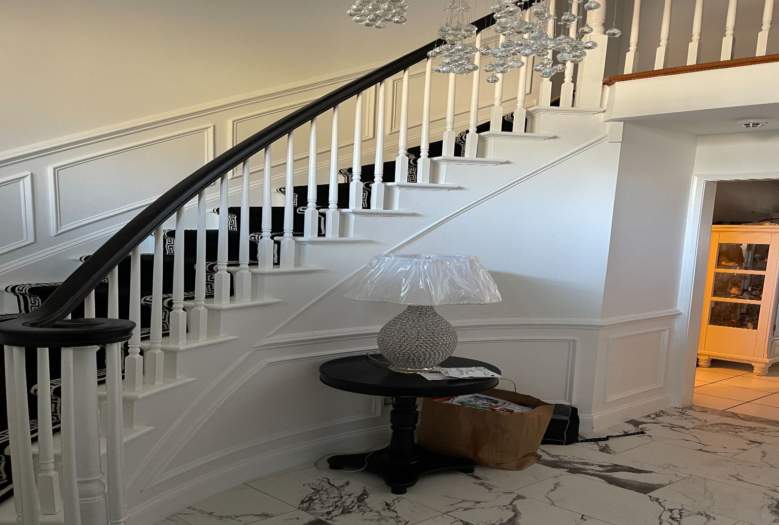 A curved staircase with a dark wooden banister and white railings, featuring a small round table with a lamp in the foyer