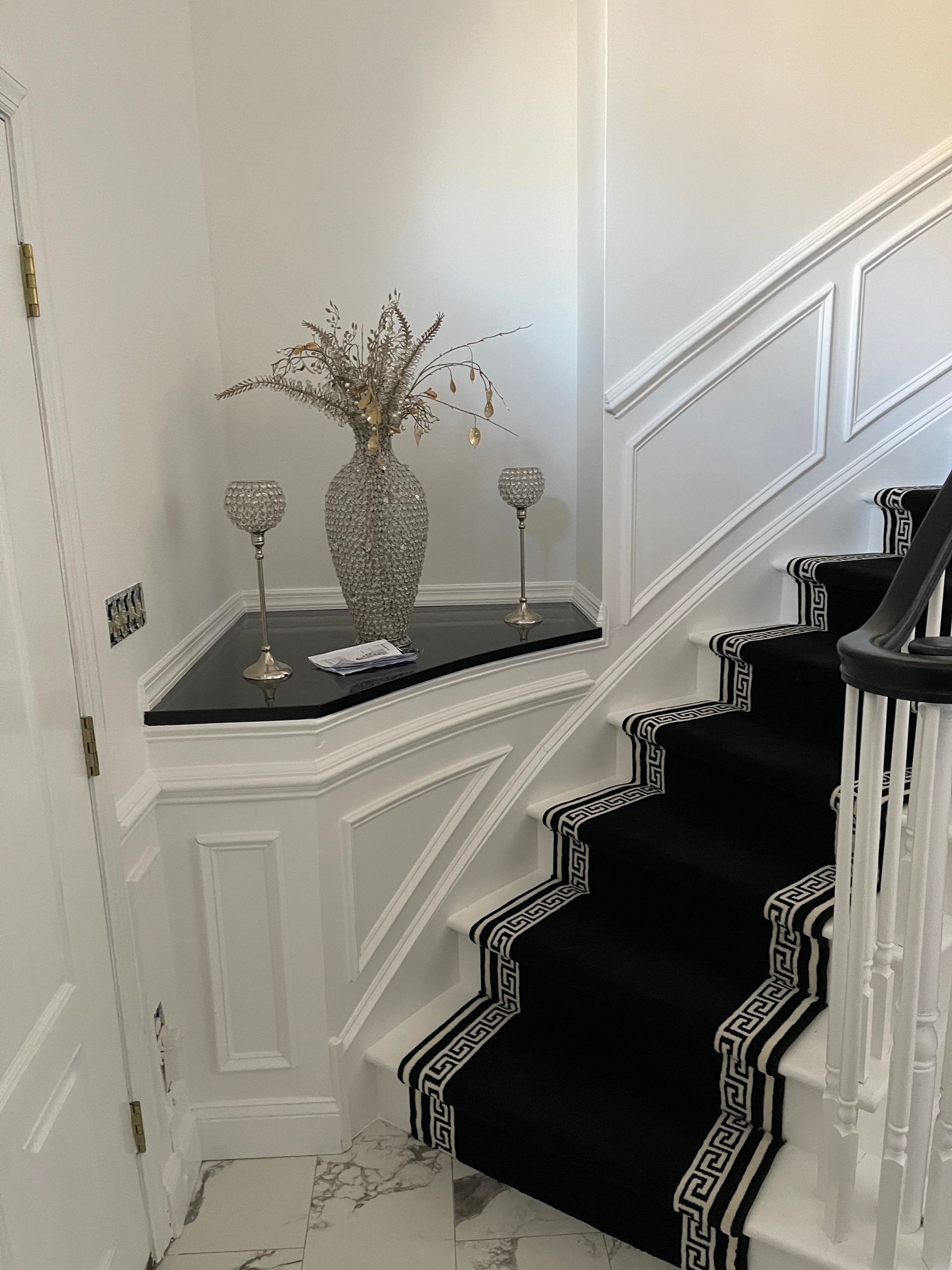 White staircase with black runner and decorative table on a landing, in a bright hallway