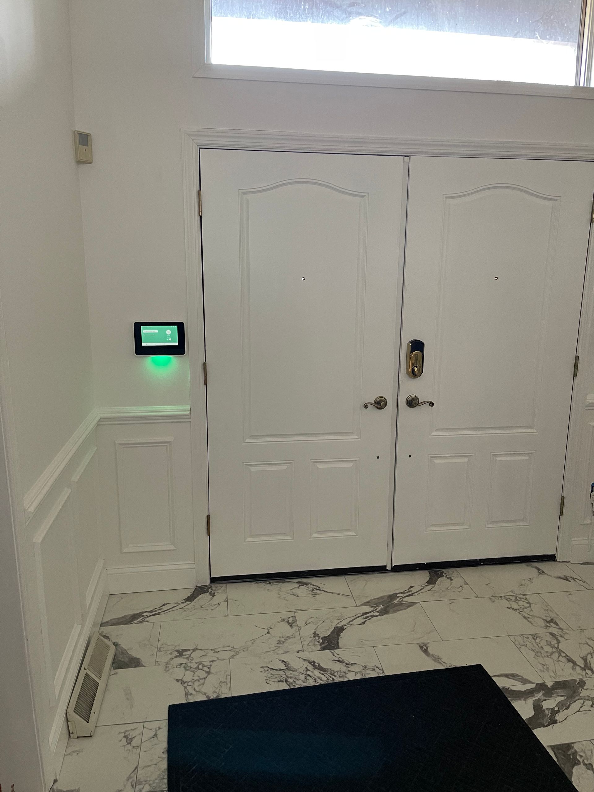 Entryway with white double doors, a wall-mounted keypad, and a black mat on a tiled floor