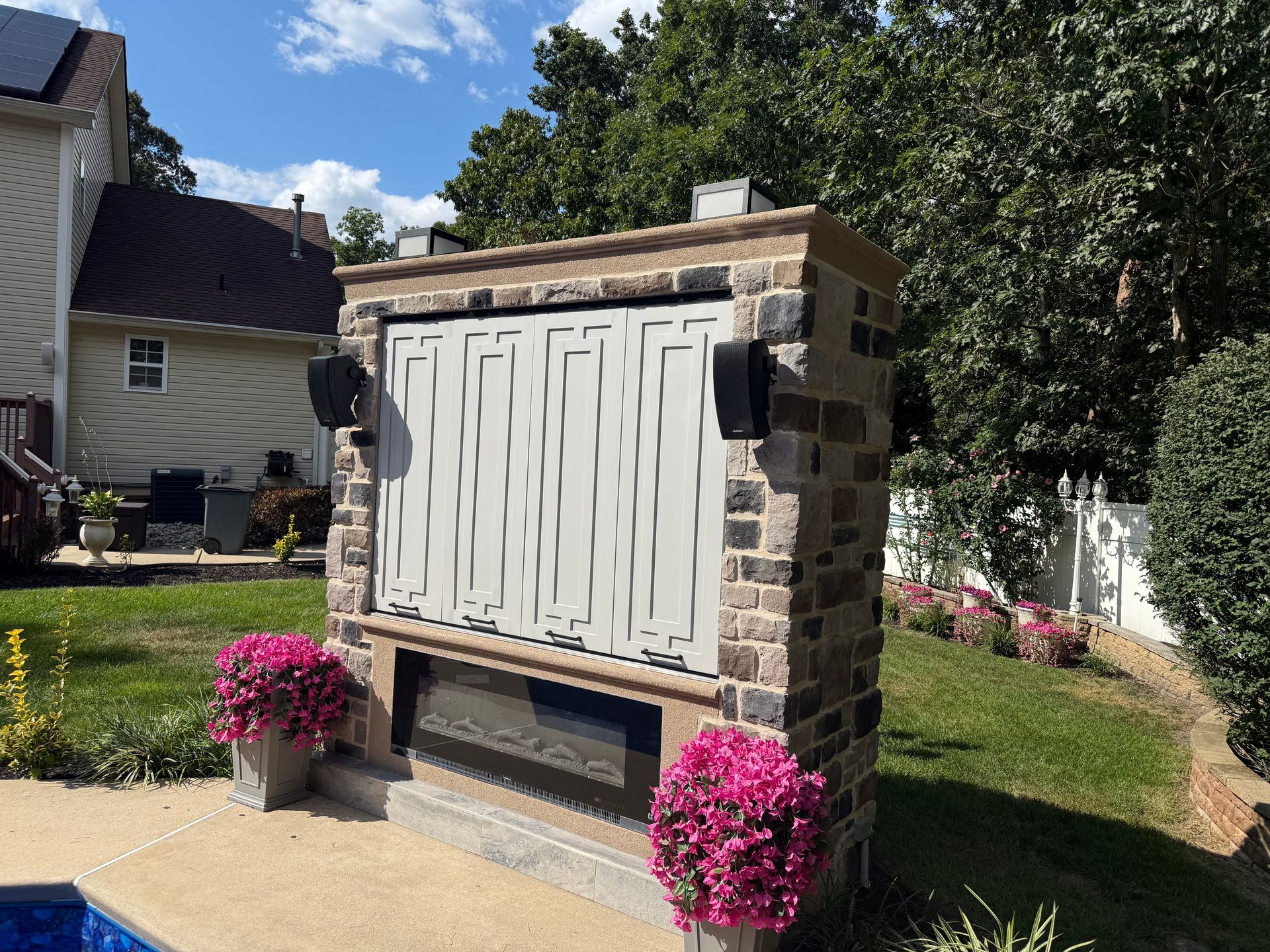 Stone mailbox with decorative white panels and pink flowers in a landscaped yard