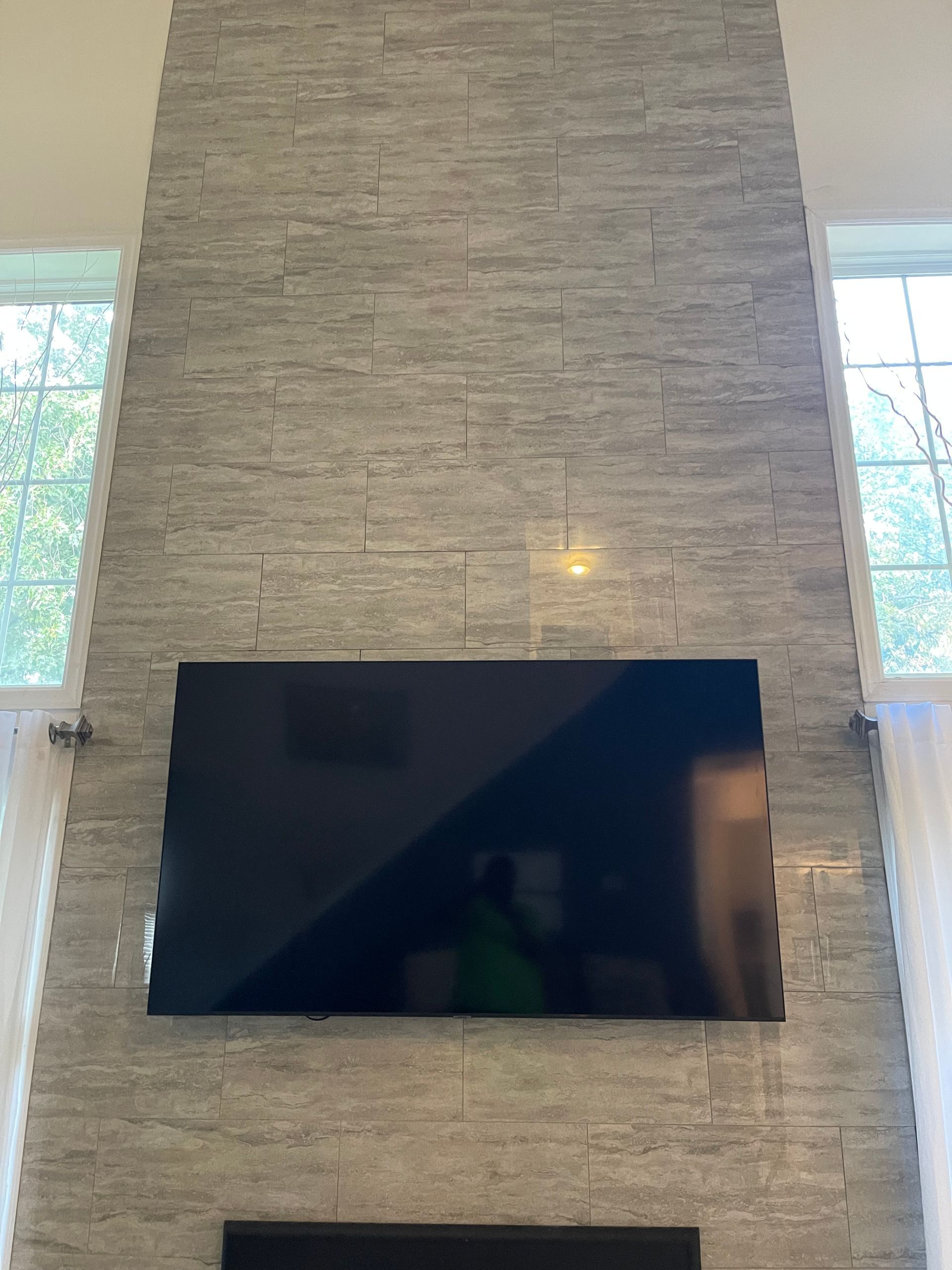 Large flat-screen TV mounted on a tall stone fireplace wall between two windows