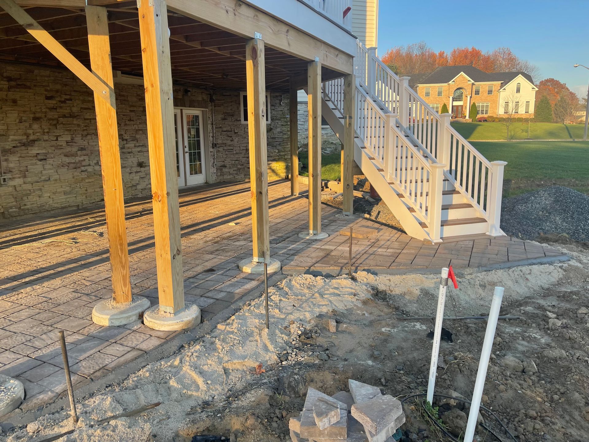 A stone patio under a wooden deck with white stairs leading up to the house and a yard in the background