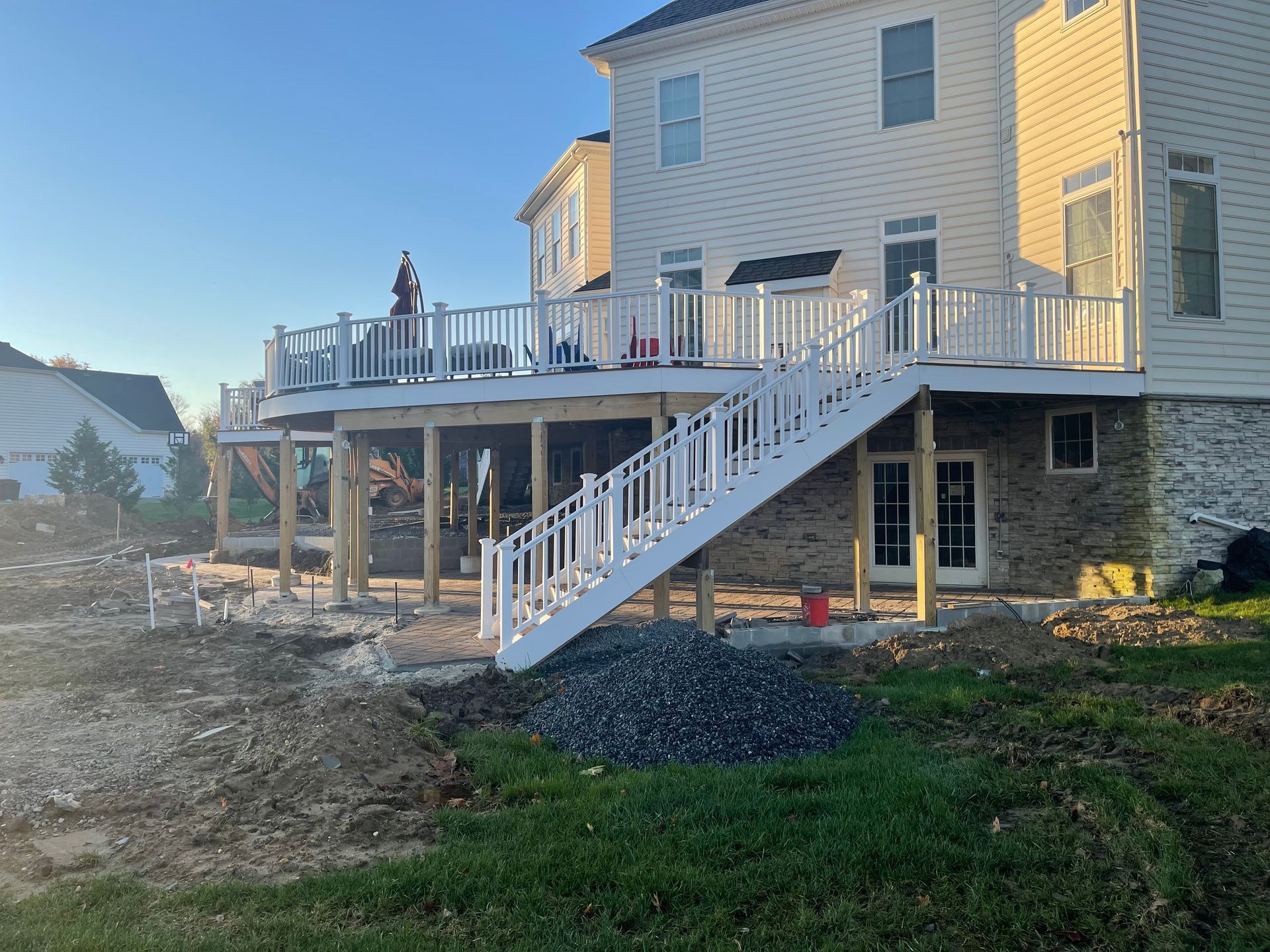 A beige house with a newly constructed white deck and staircase overlooking a backyard undergoing landscaping