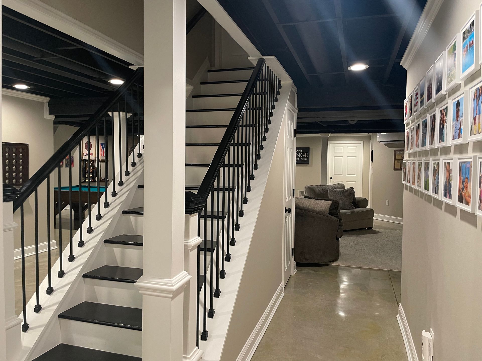 Modern hallway with two staircases, gray carpet runner, and framed photos on white walls