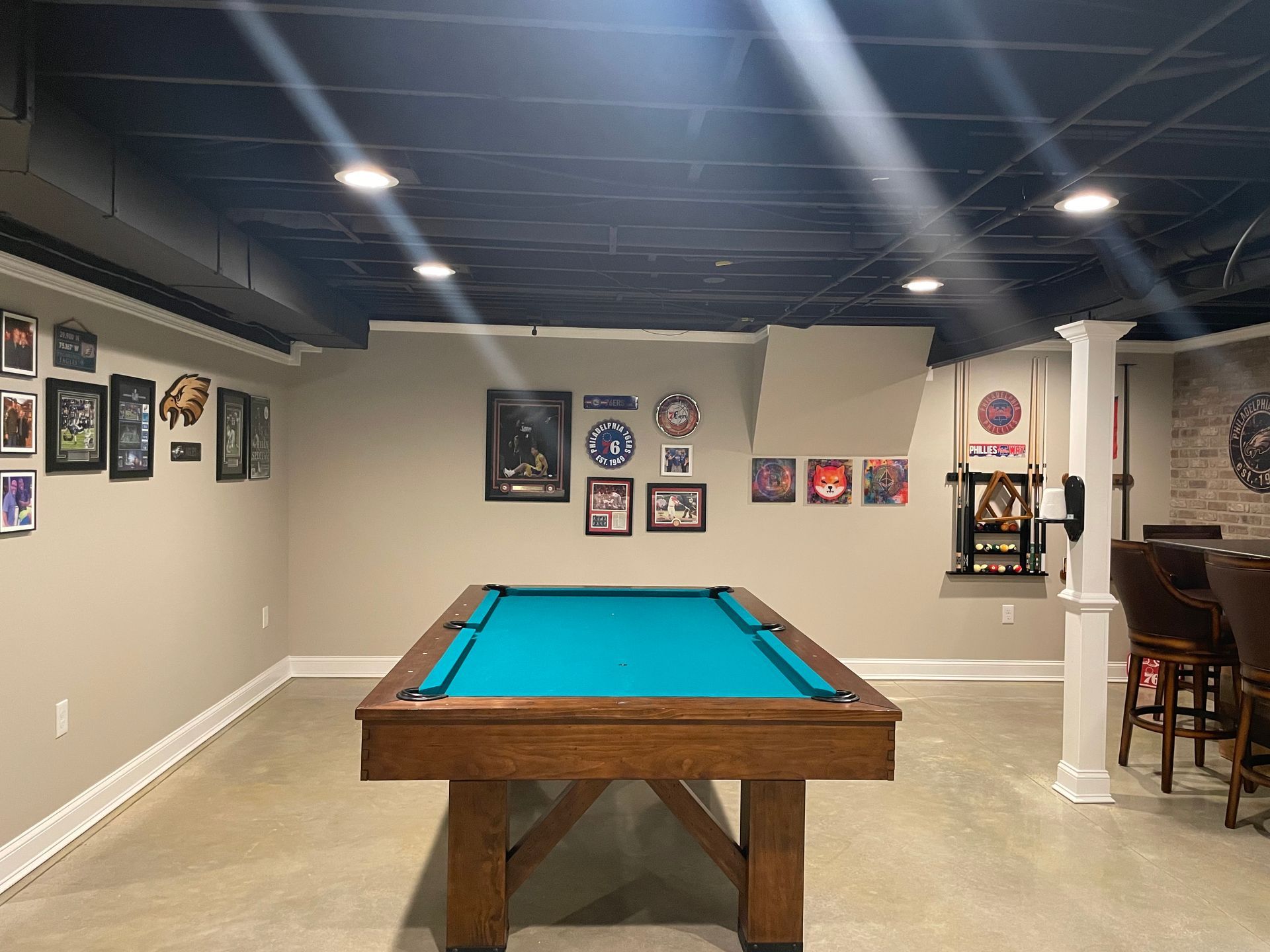 Basement game room with a blue pool table centered under recessed lights