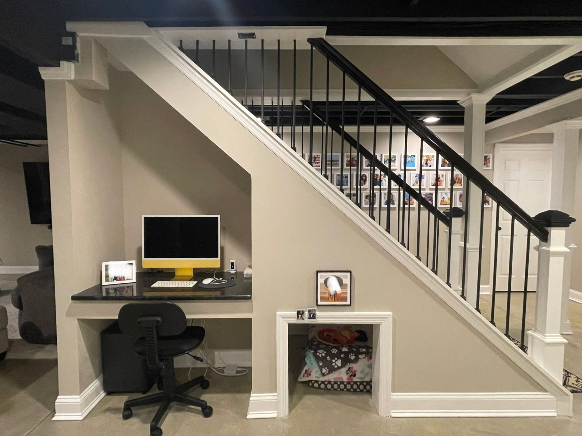 Home office nook under a staircase with desk, computer, chair, and a small pet bed below