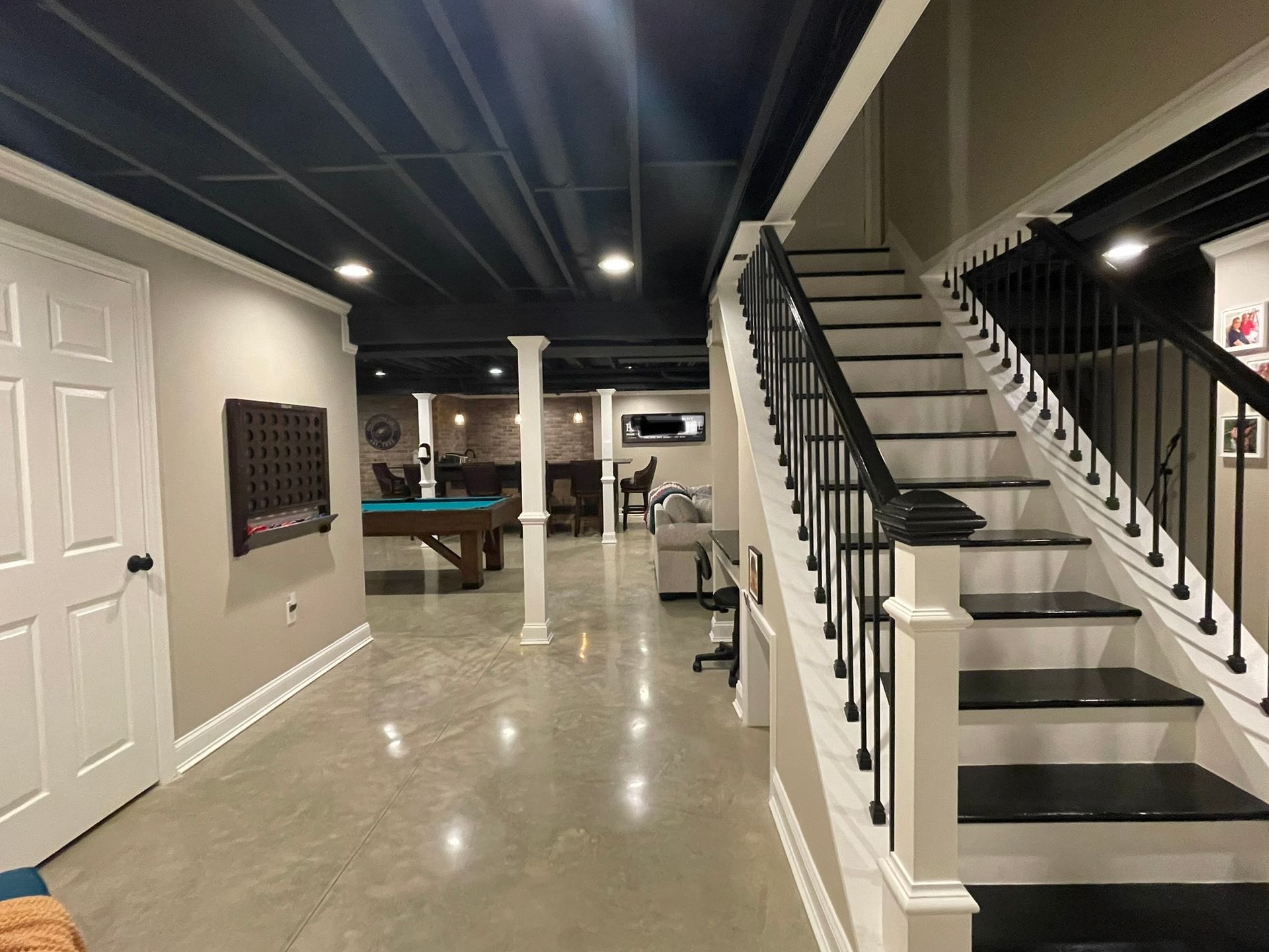A finished basement featuring a staircase with black treads, white risers, a pool table, and a black open-joist ceiling