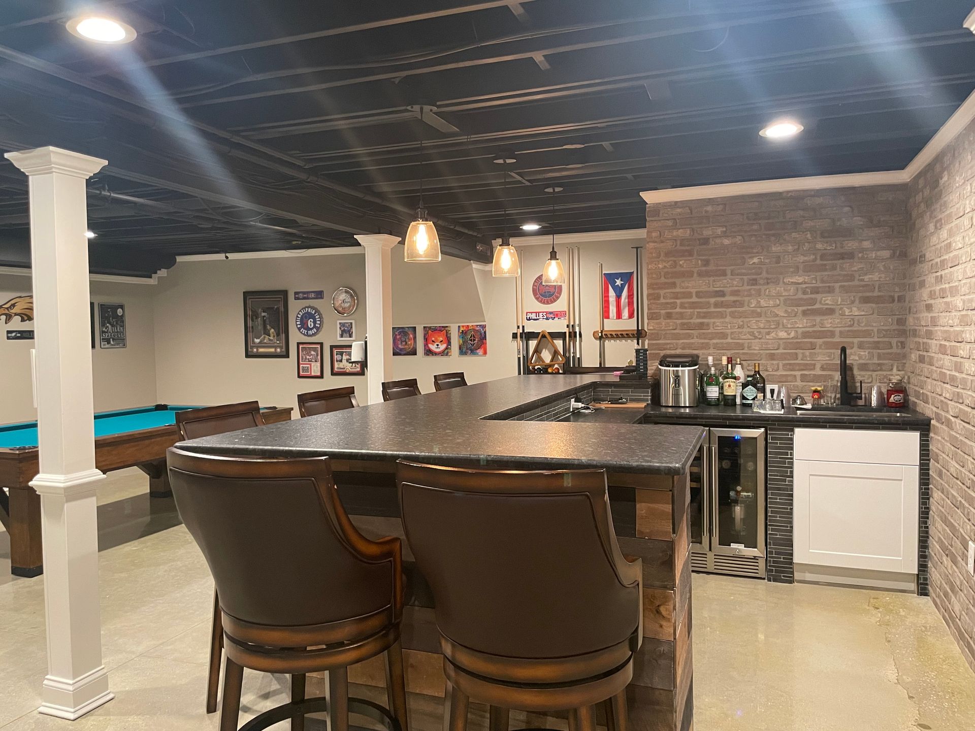 Home basement bar with granite counter, stools, pool table, and brick accent wall