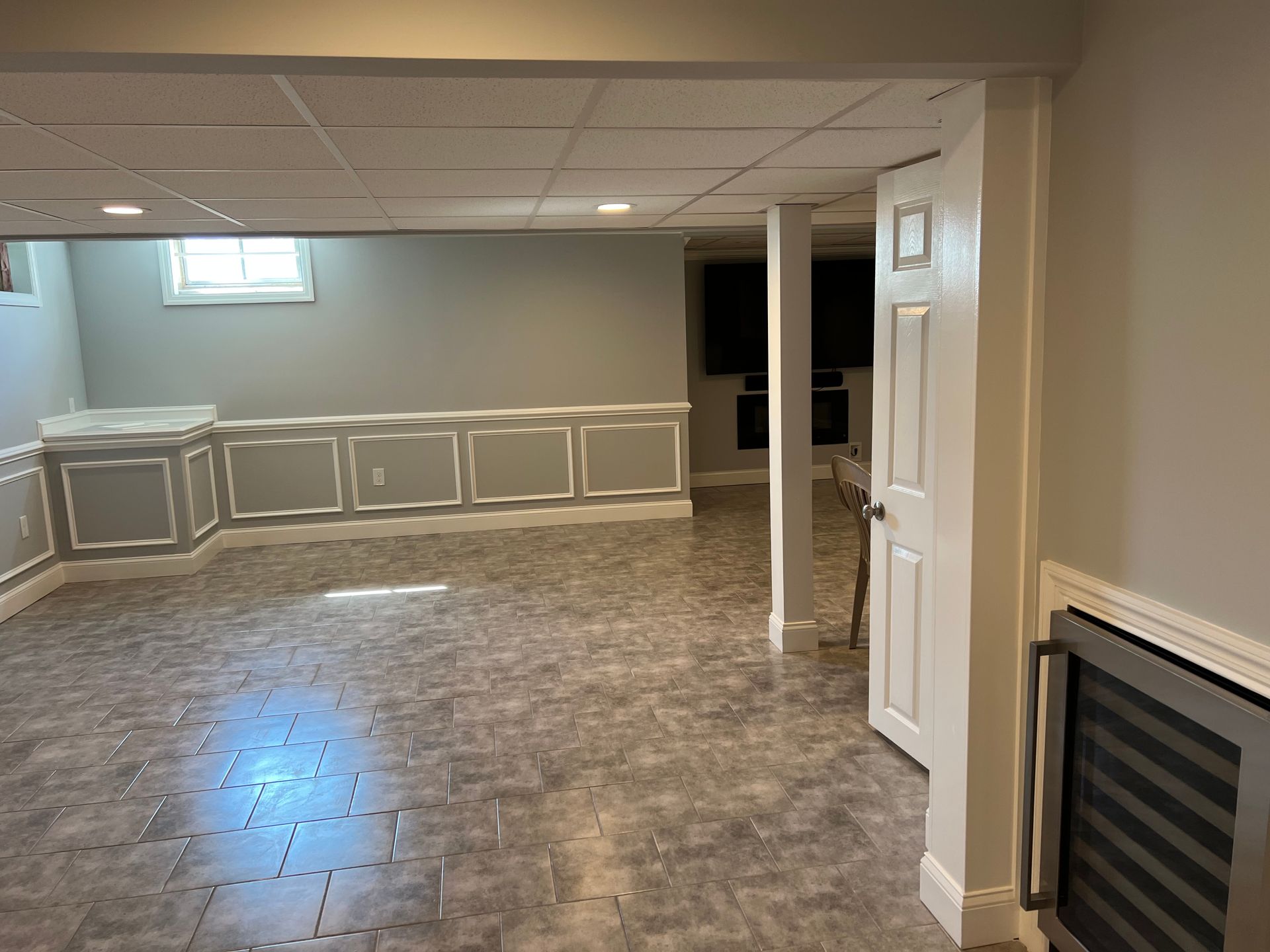 Empty basement room with tiled floor, beige walls, built-in cabinets, and a white support column