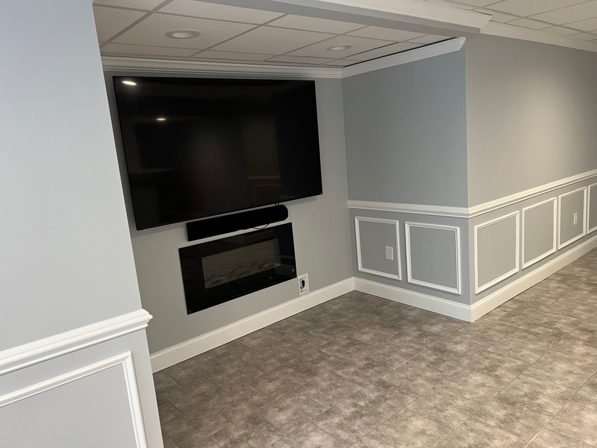 Basement media room with wall-mounted TV and fireplace, gray walls, white trim, and carpeted floor