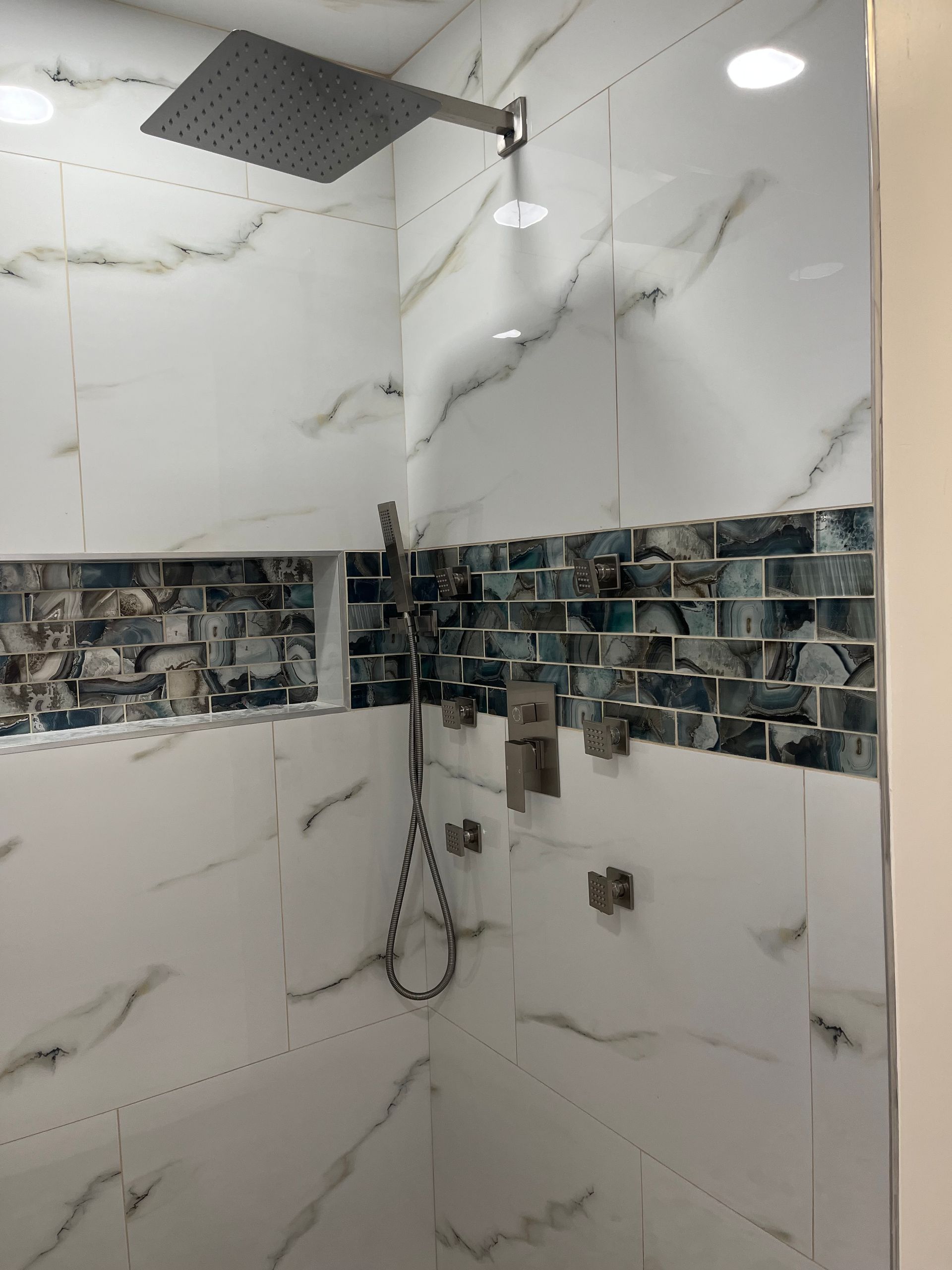 Modern tiled shower with rainfall showerhead, handheld sprayer, and blue decorative border tiles