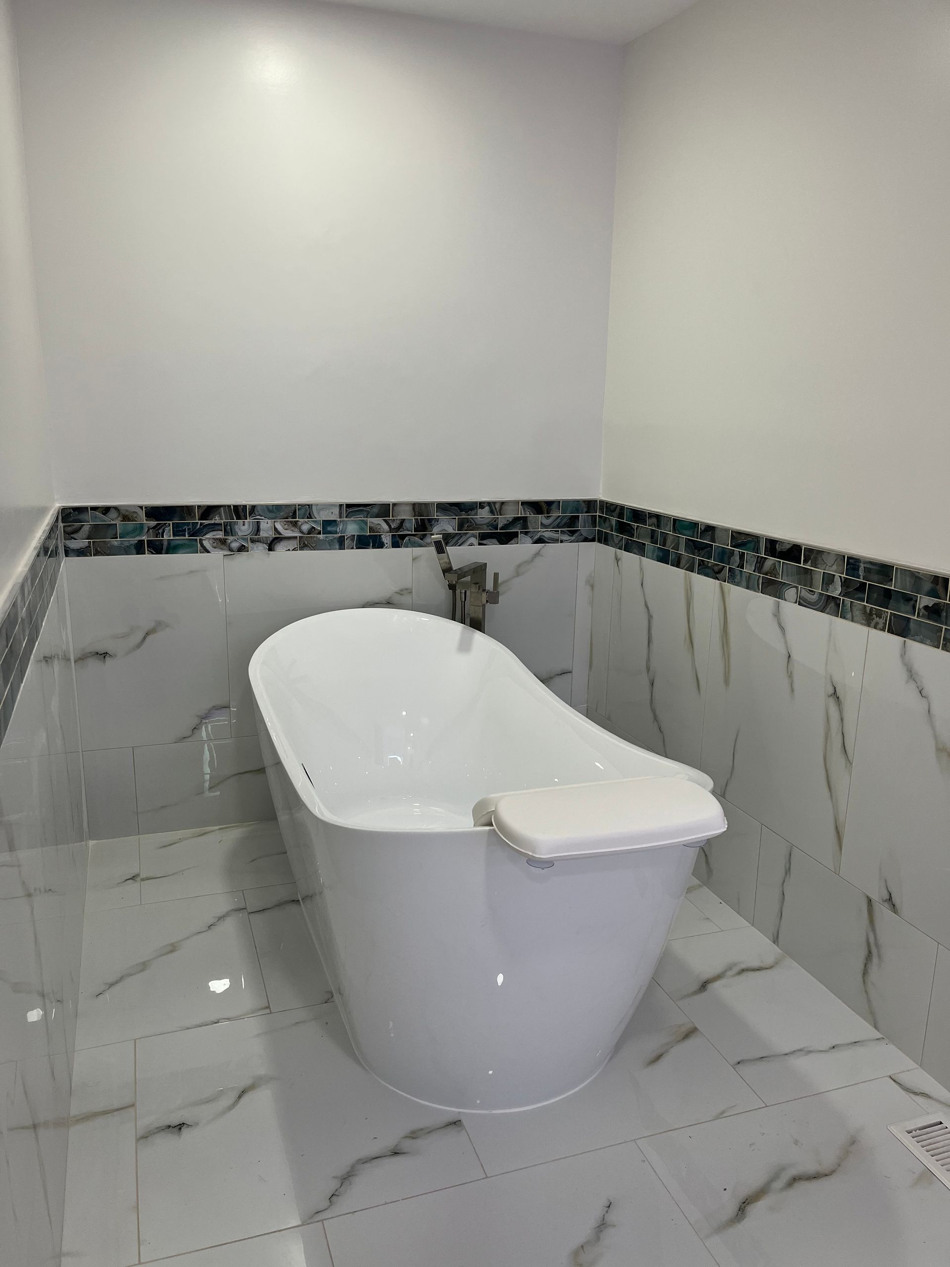 Modern bathroom with a white bathtub and glossy white marble-patterned tile walls and floor