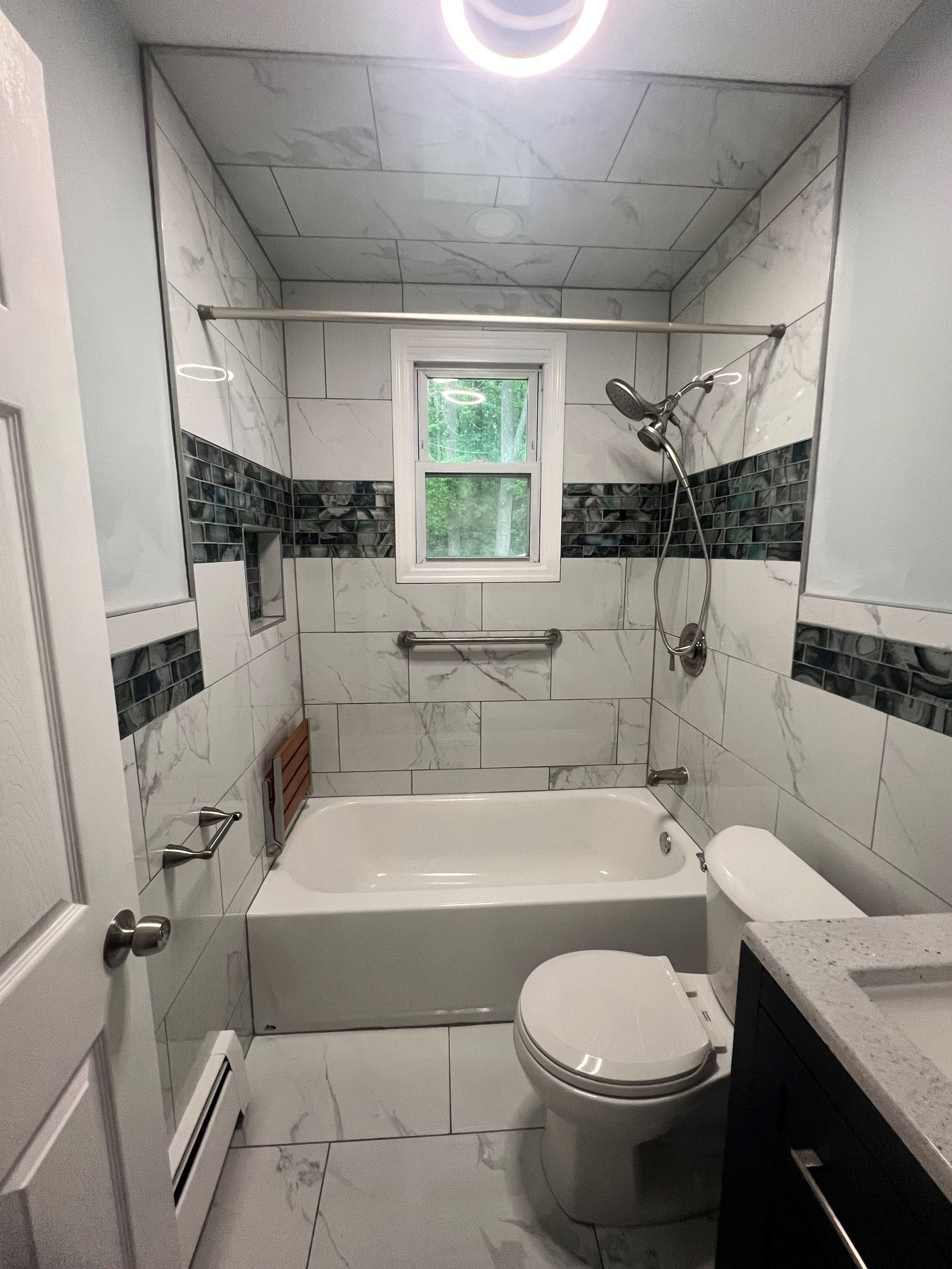 Small bathroom with white tile, bathtub, toilet, sink, and a window above the tub