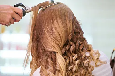 Hairdresser curling long blonde hair with a curling iron in a salon