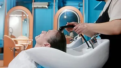 Person receiving a shampoo bowl rinse at a salon, with stylist holding a spray nozzle.