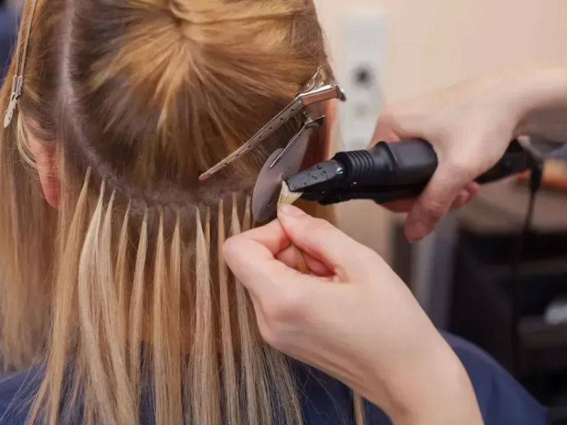 Stylist using a curling iron to style blonde hair with hair clips in a salon