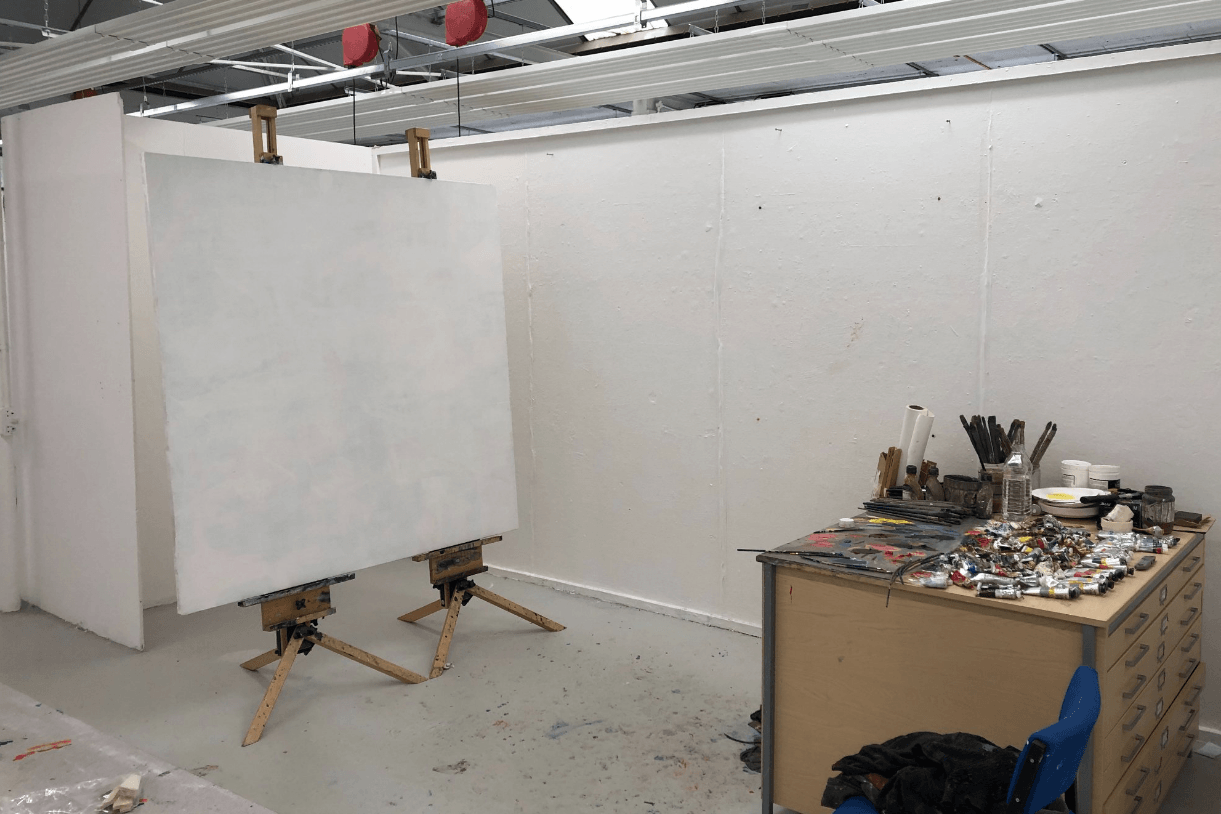 A blank canvas on an easel in a bright studio with paint supplies.