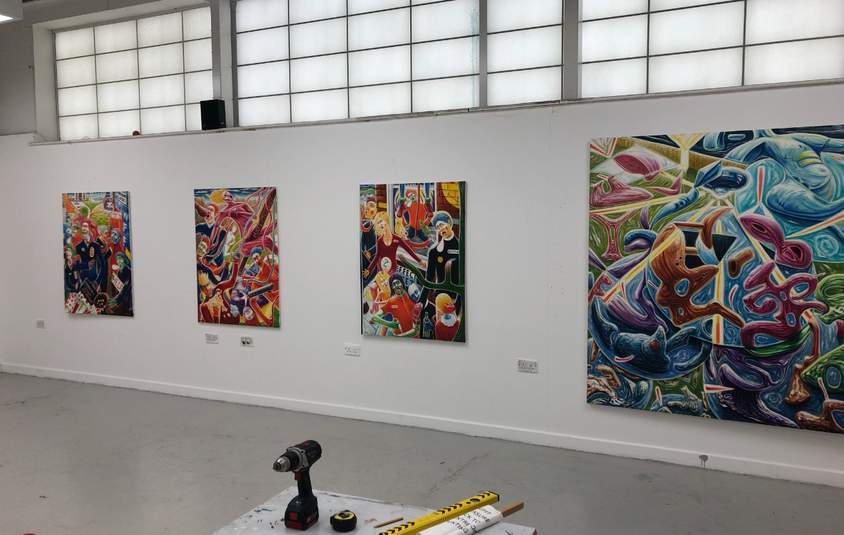 Art gallery wall with four colorful abstract paintings displayed in a bright white room.