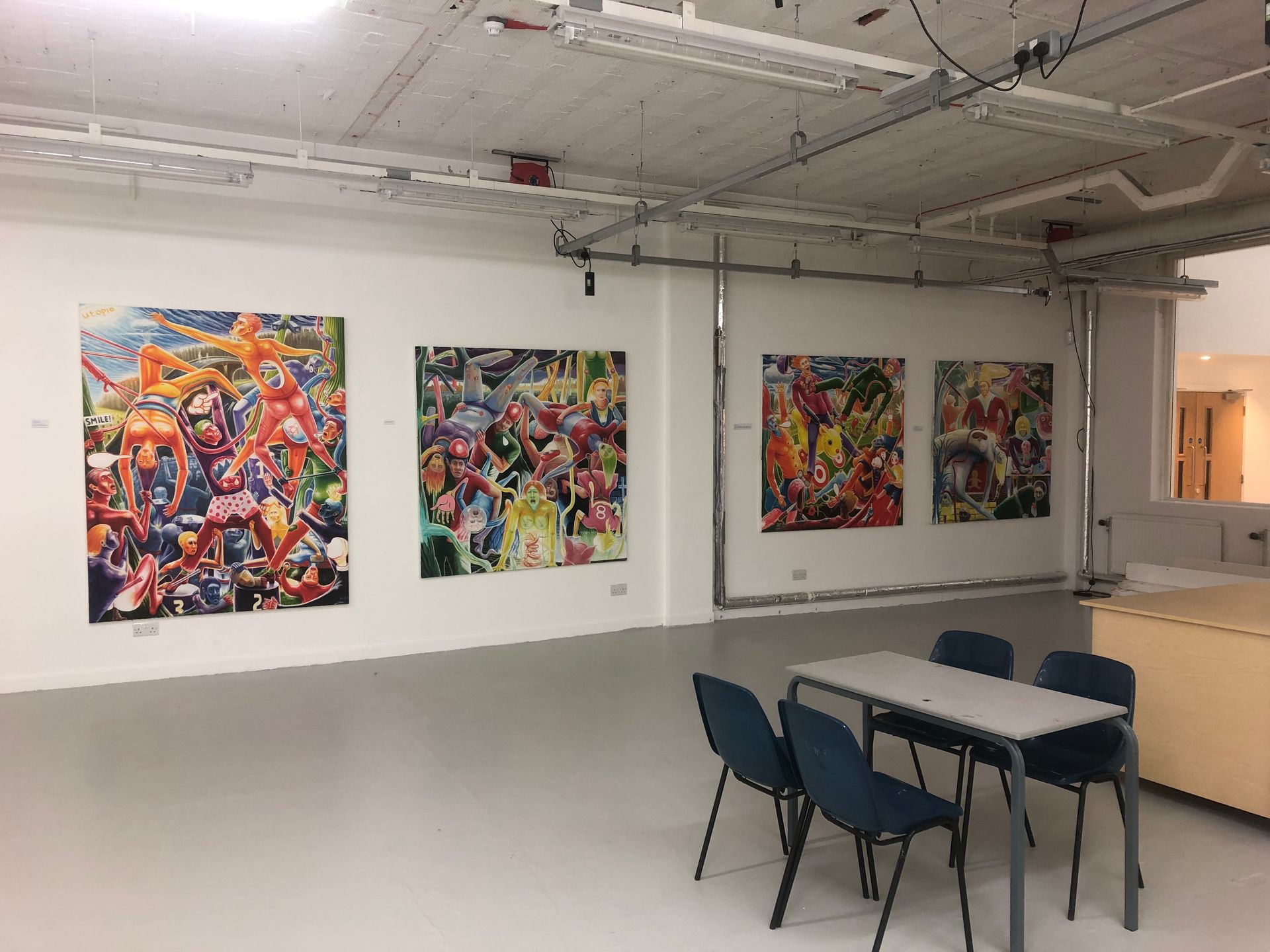 Art gallery with colorful abstract paintings on white walls, table with chairs in front.
