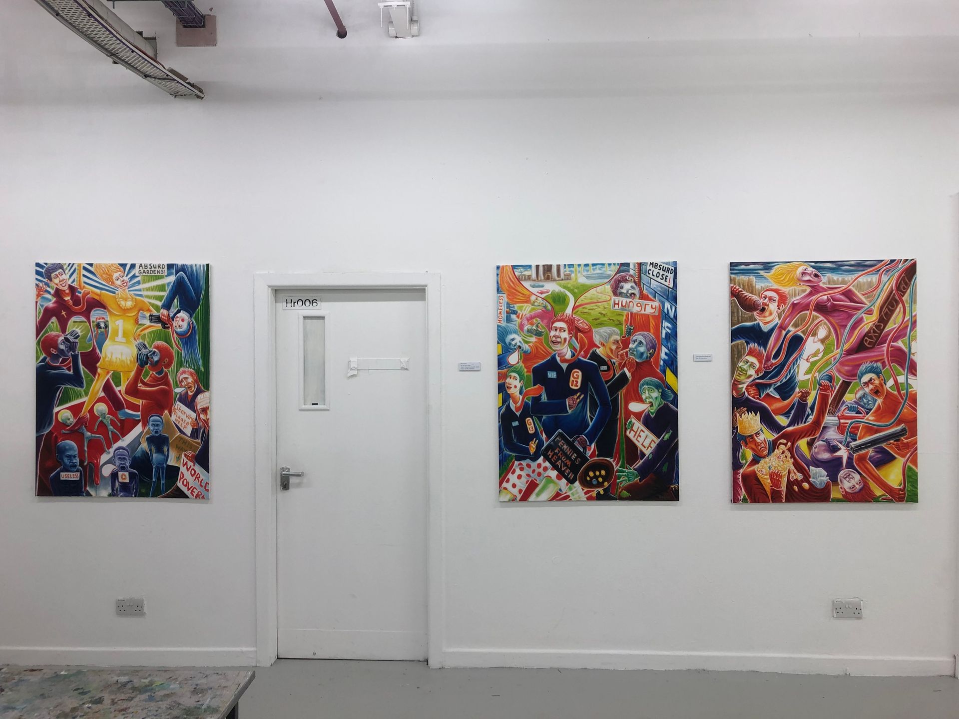 Three colorful paintings hang on a white wall. A white door is between the second and third painting.