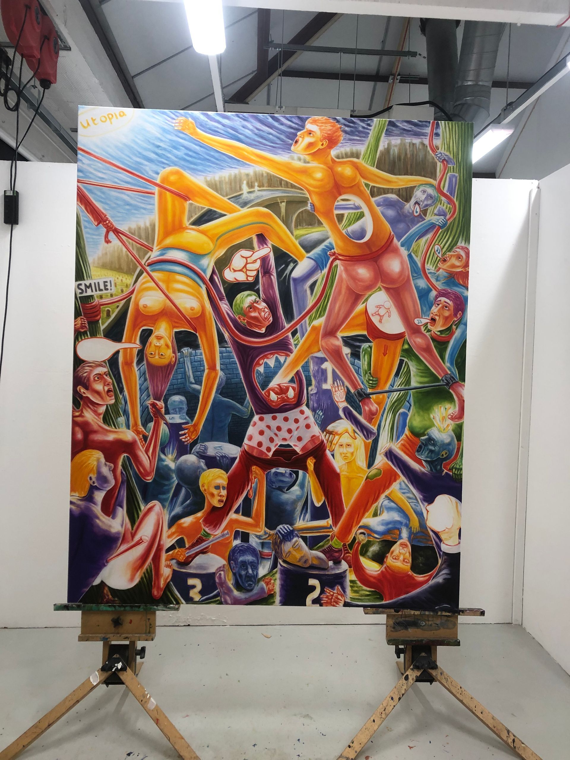 Large colorful abstract painting on an easel in a studio, with bright figures and swirling shapes