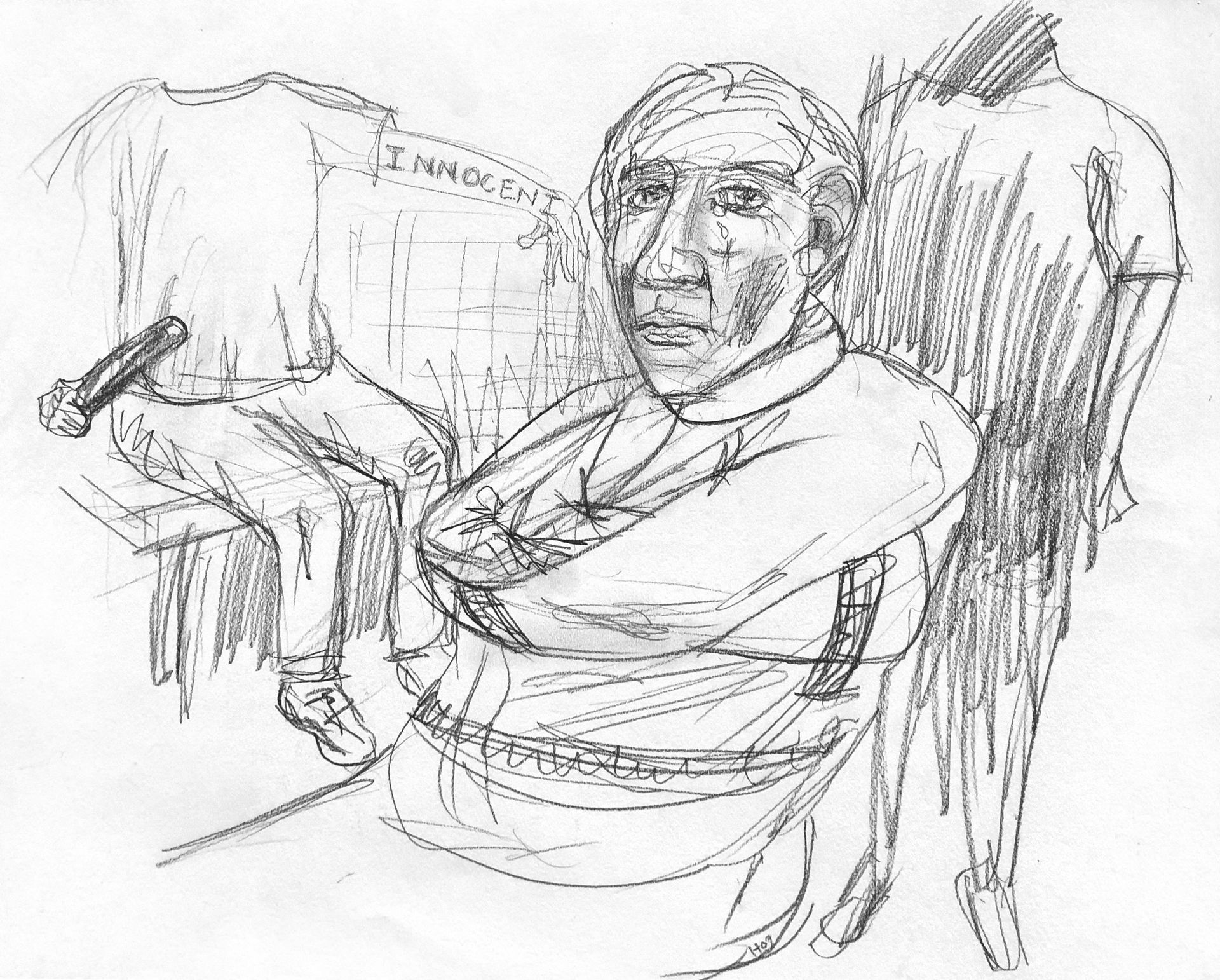 A person with arms crossed, sitting with two hanging shirts behind. One shirt reads
