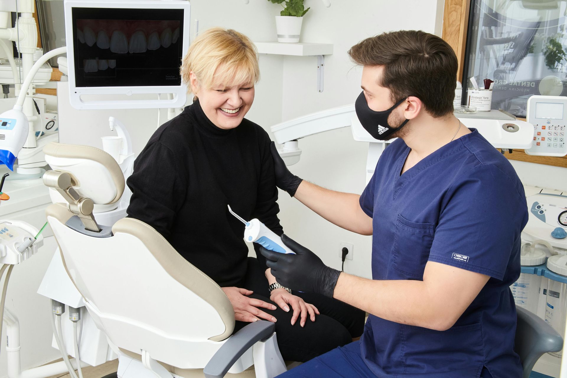 Dentist sitting with patient, explaining how a procedure works and holding a tool for cleaning