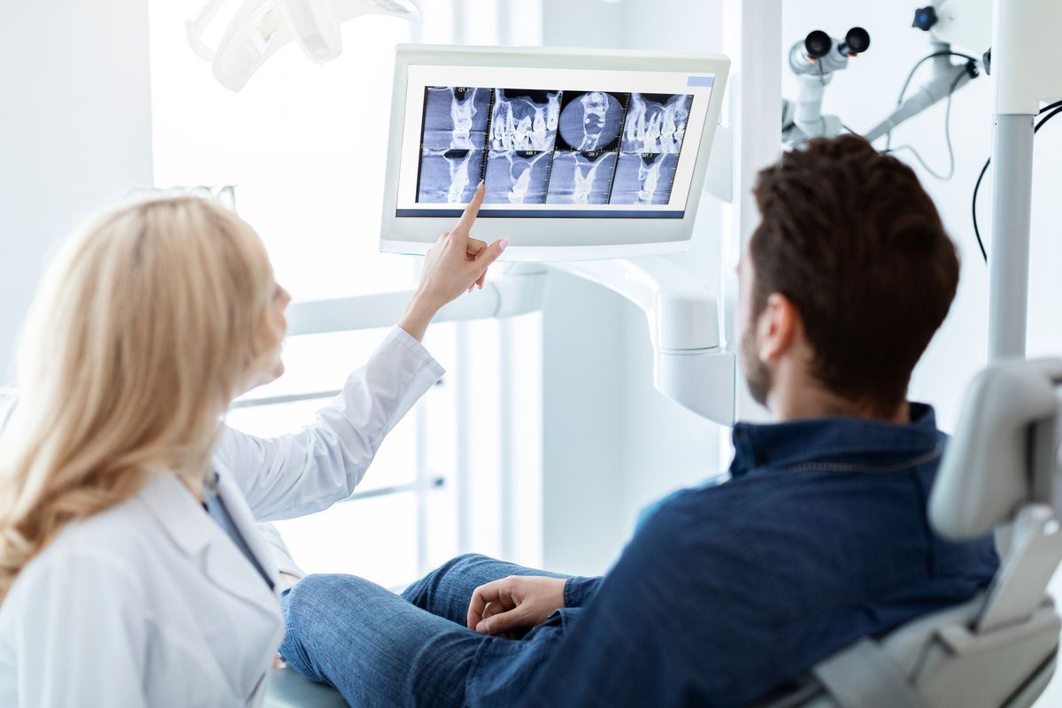 Dentist points to X-ray on a monitor while patient reclines in a dental chair