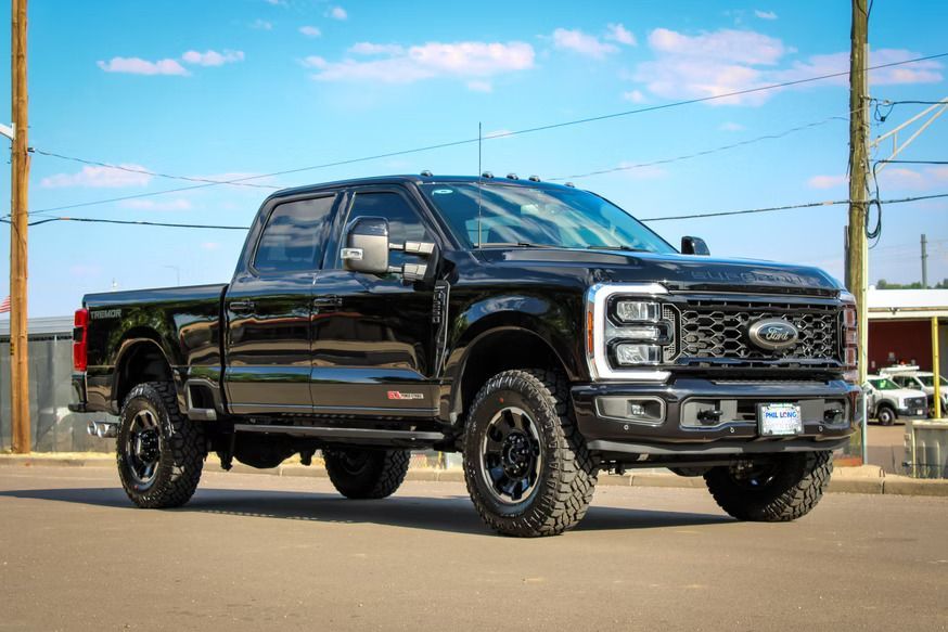 A black Ford Super Duty pickup truck parked on an asphalt lot under a blue sky.