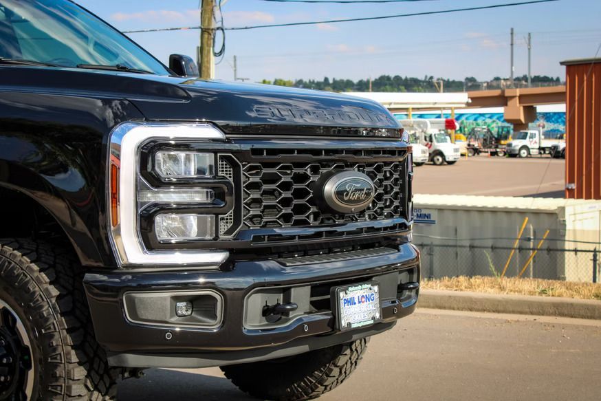 Close-up front view of a black Ford Super Duty truck with distinctive C-shaped LED headlights, parked on an asphalt lot.