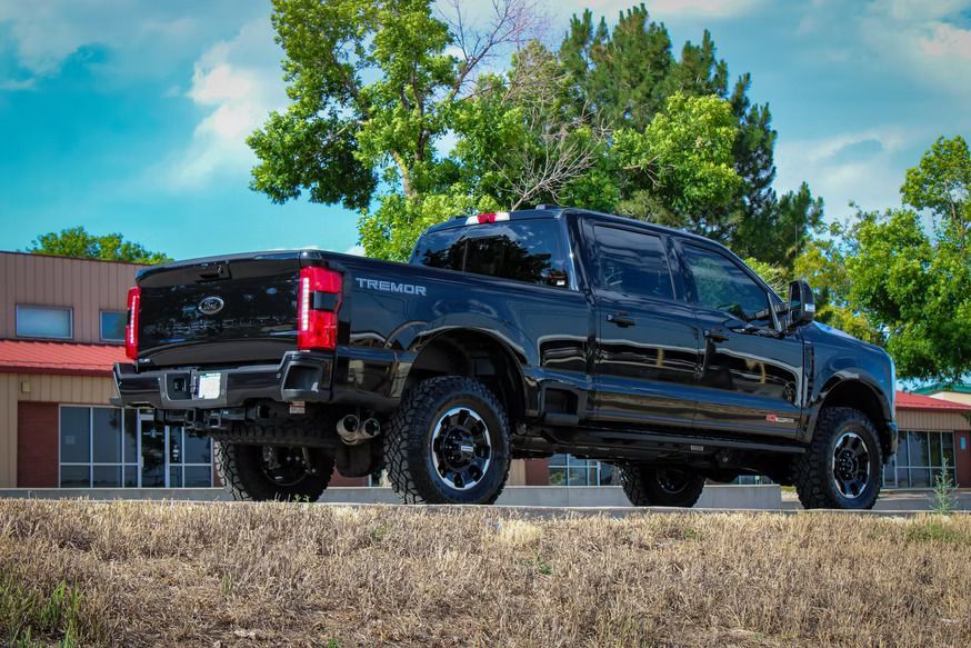 A black Ford Super Duty Tremor pickup truck parked on a dry, grassy slope in front of a building and trees.