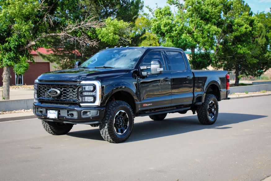 A black Ford Super Duty crew cab pickup truck parked on a paved road with trees in the background.