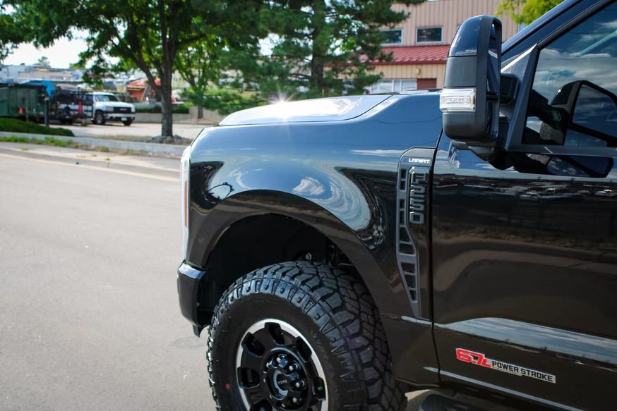 A close-up view of the front quarter panel, wheel, and side mirror of a black Ford Super Duty truck parked on a street.