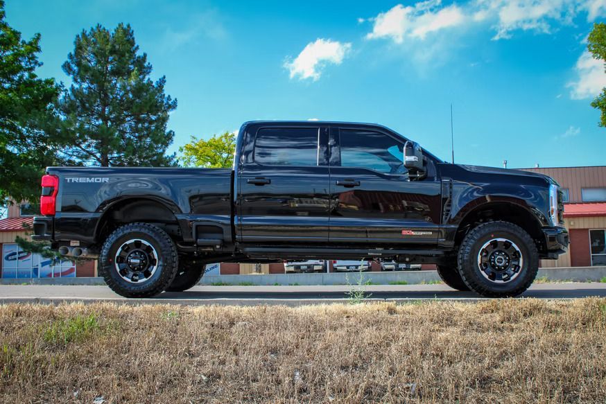 Black pickup truck parked in profile on a sunny day with a building and trees in the background.