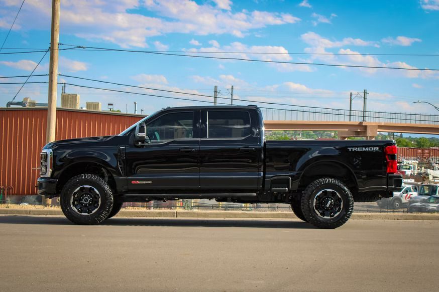 A black Ford Super Duty pickup truck parked on an asphalt lot under a blue, cloudy sky.