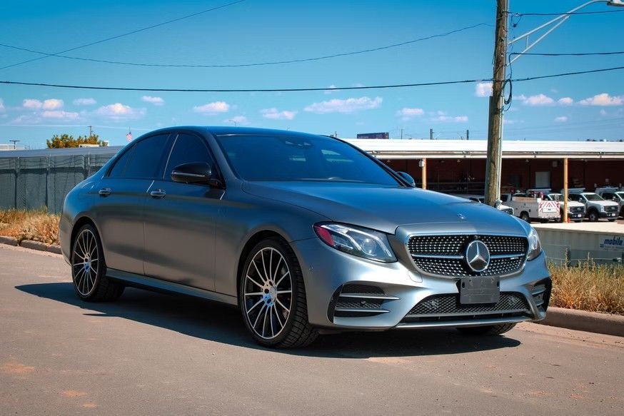 A gray Mercedes-Benz sedan parked on a paved road under a clear blue sky.
