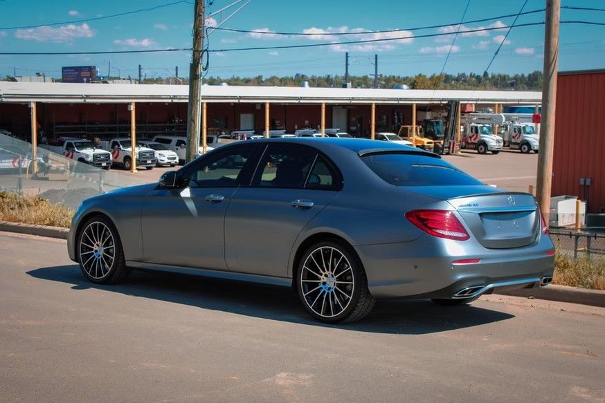 A grey Mercedes-Benz sedan parked on a paved lot with a covered storage structure in the background.