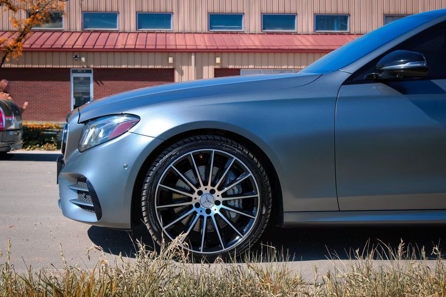 A side view of a metallic grey sedan parked outdoors, highlighting its multi-spoke alloy wheels and sleek design.