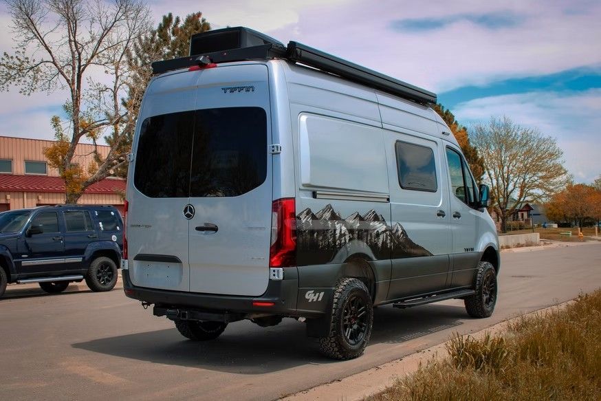 Silver camper van with mountain graphics and off-road tires parked on an asphalt street.
