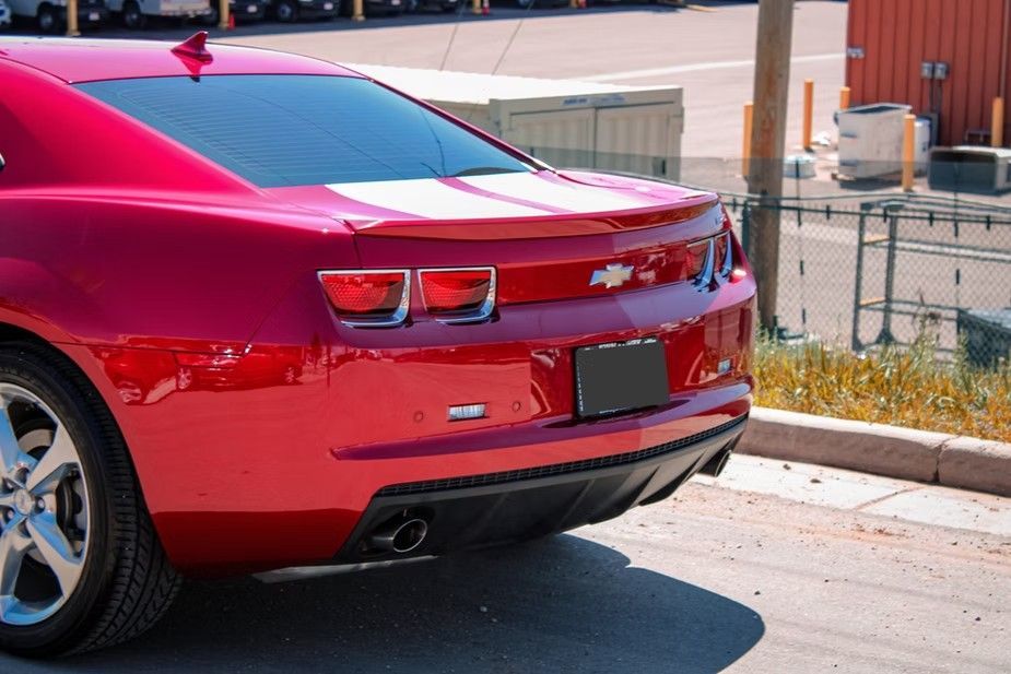 A bright red Chevrolet Camaro parked outdoors, showcasing its rear taillights, spoiler, and exhaust pipes.