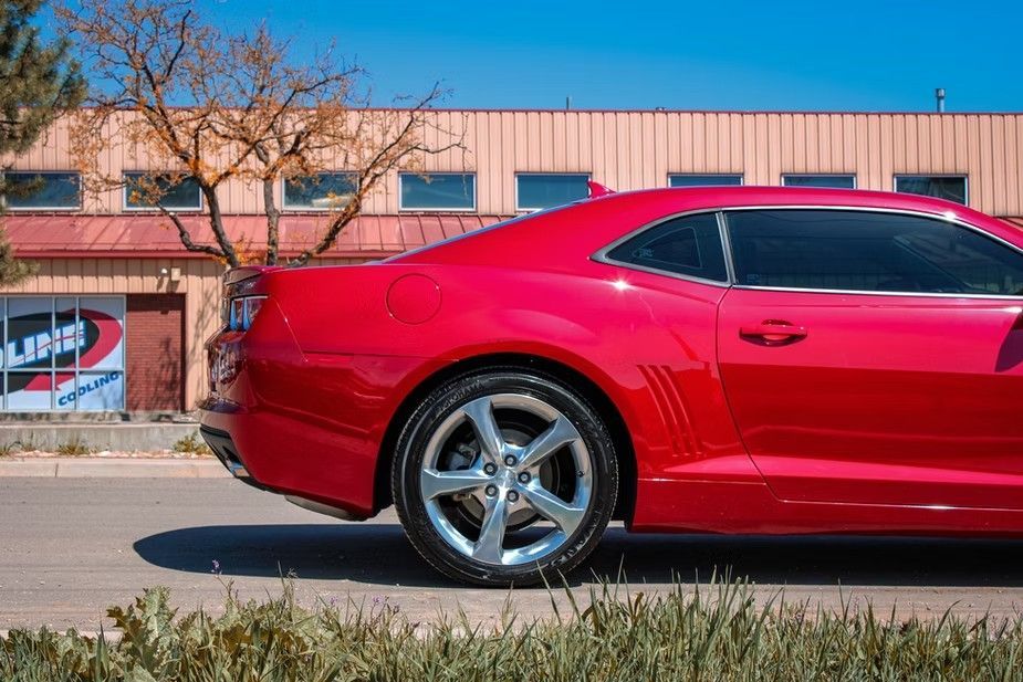 A side view of a bright red sports car parked outside a building on a sunny day.