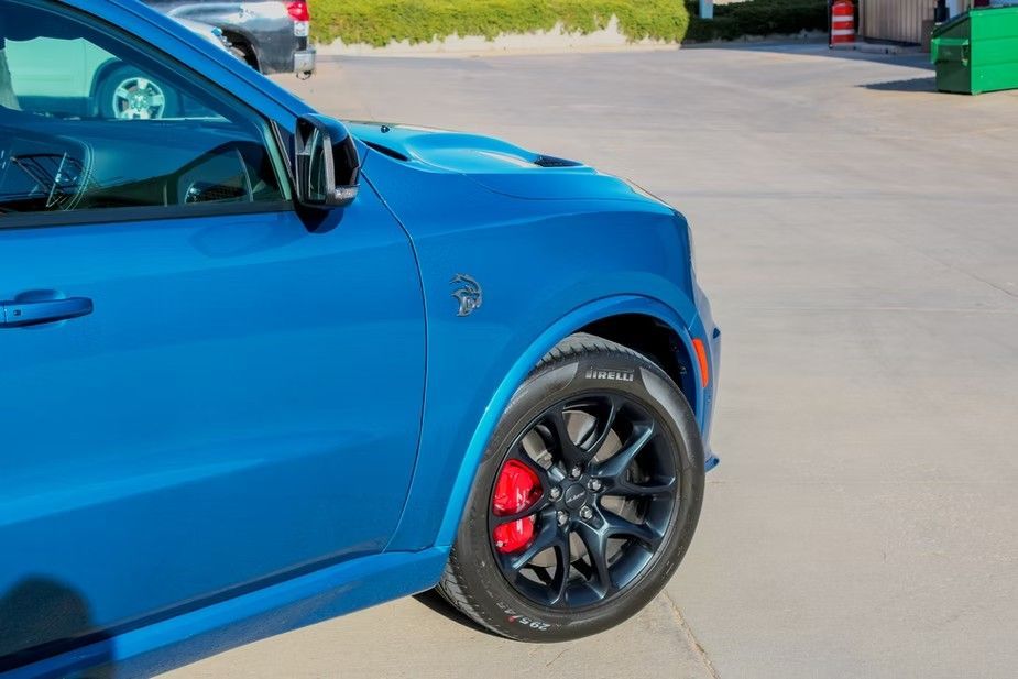 A close-up of a blue SUV's front fender featuring a circular emblem, black wheels, and bright red brake calipers.