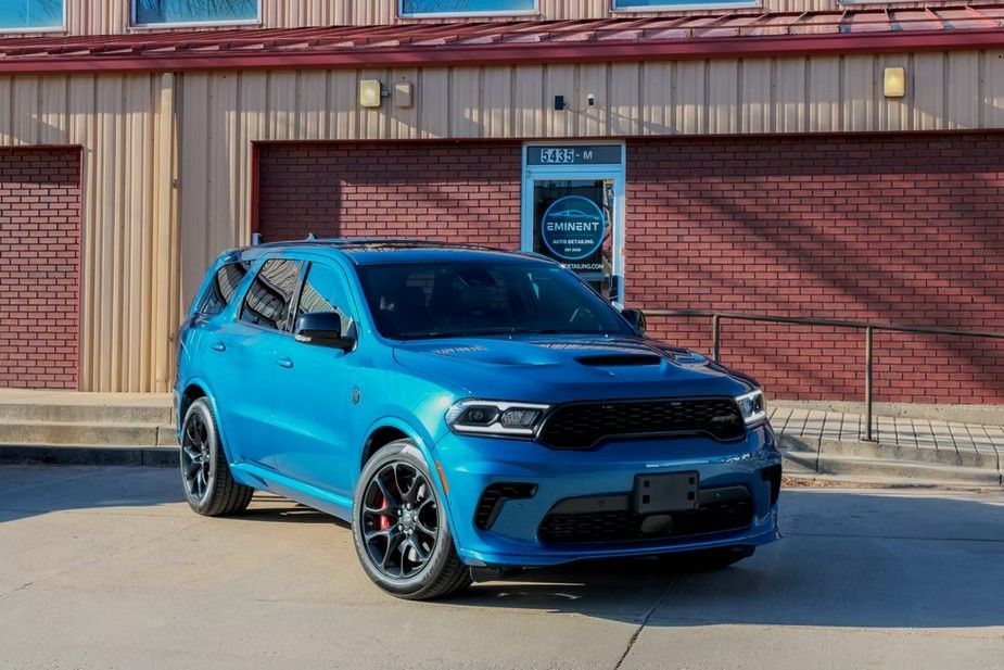 A bright blue Dodge Durango parked on a concrete lot in front of a brick building.