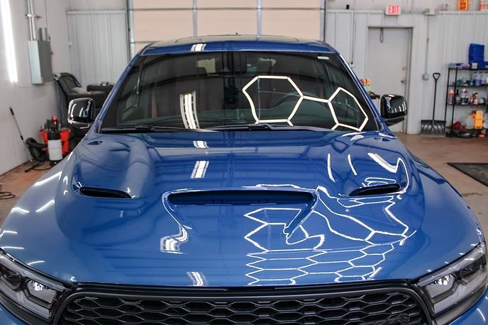 A blue Dodge Durango with a hood scoop parked inside a brightly lit automotive workshop.