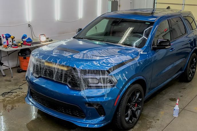 A blue Dodge SUV in a garage, partially covered in clear protective film during an auto detailing process.