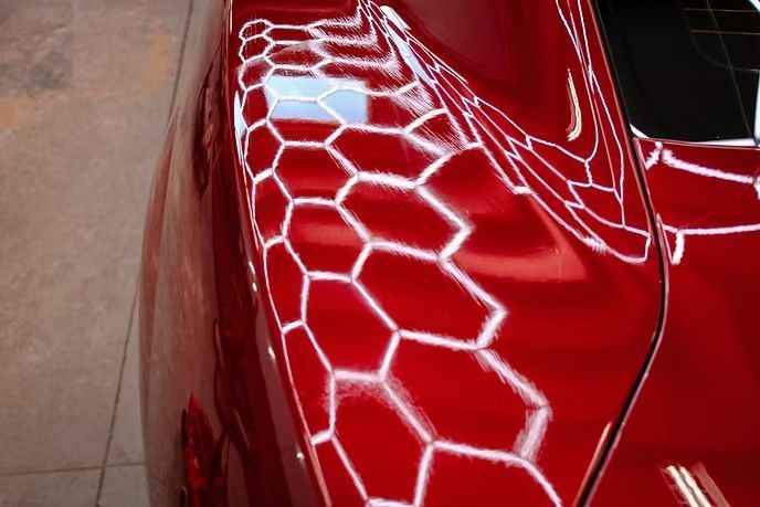 A red car panel showing a hexagonal light reflection pattern used for paint inspection.