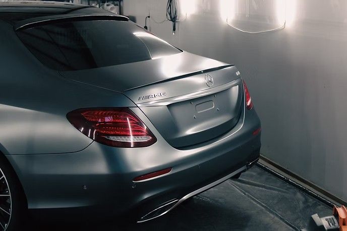 A matte grey Mercedes-Benz sedan parked in a garage with studio lighting reflecting on its trunk and rear light.