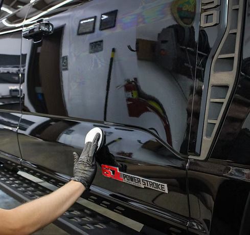 A person in a black glove uses a circular polishing pad on the shiny black exterior of a truck with a Power Stroke badge.