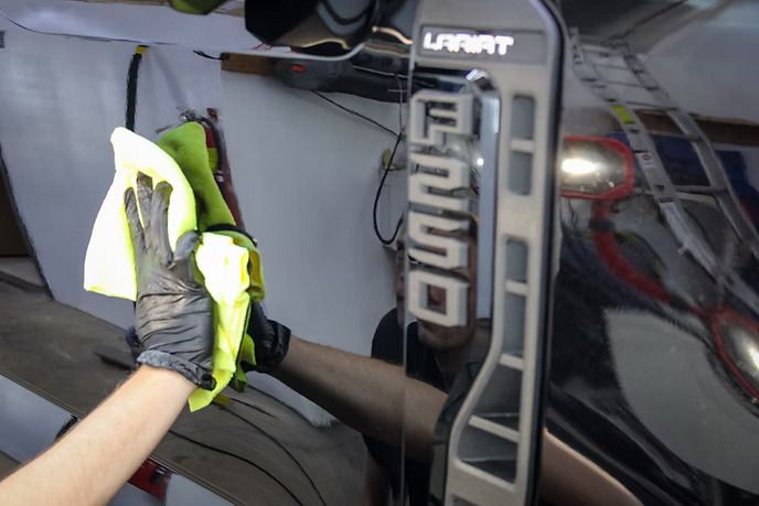 A gloved hand uses a yellow microfiber cloth to wipe the side of a black Ford F-250 Lariat truck.